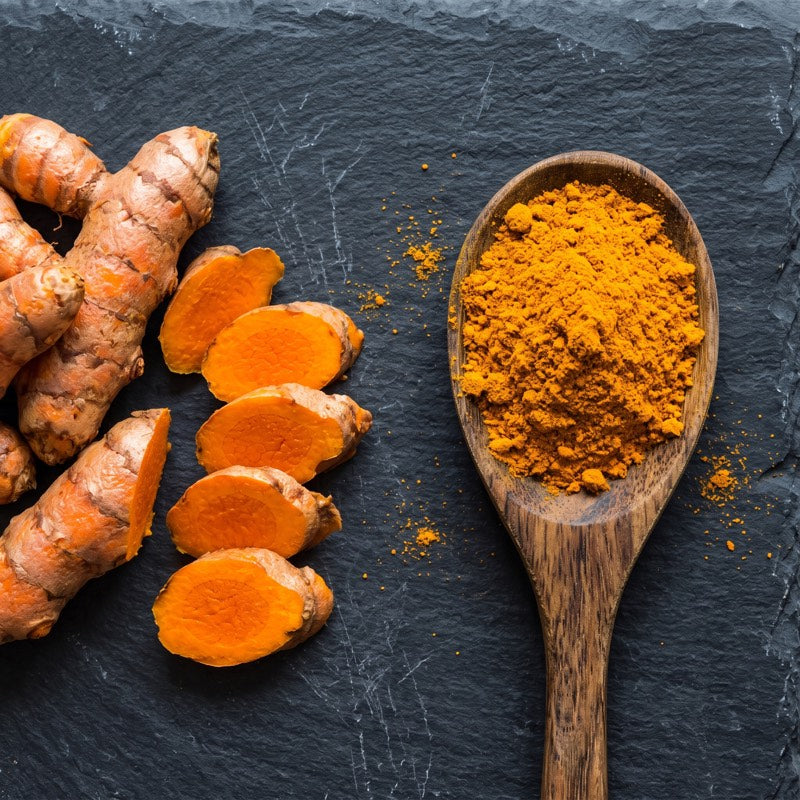 Turmeric capsules beside fresh turmeric root on a kitchen counter